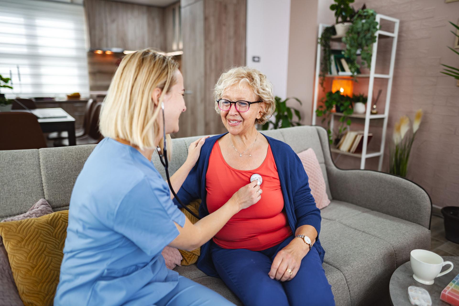 Nurse examining senior woman with stethoscope at home